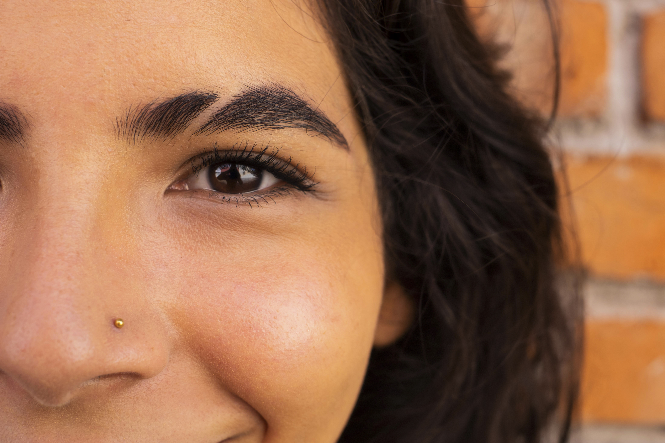 Close-up shot of a smiling person with a nose piercing and well-groomed eyebrow, facing the camera