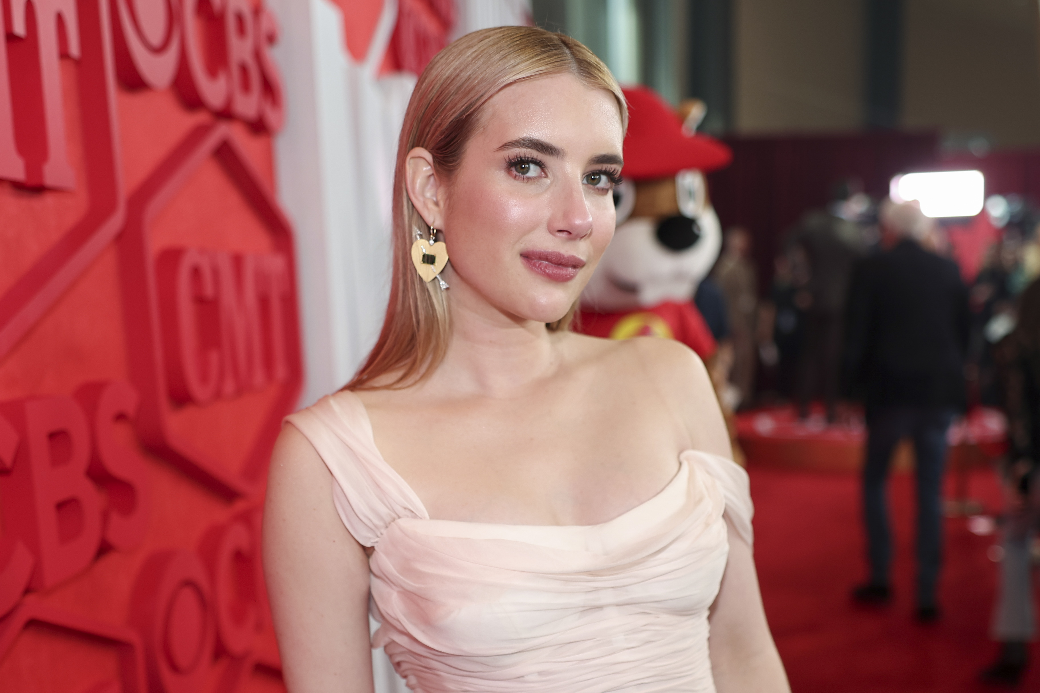 Emma Roberts wearing a stylish off-shoulder gown with drop earrings on the red carpet, posing for photos