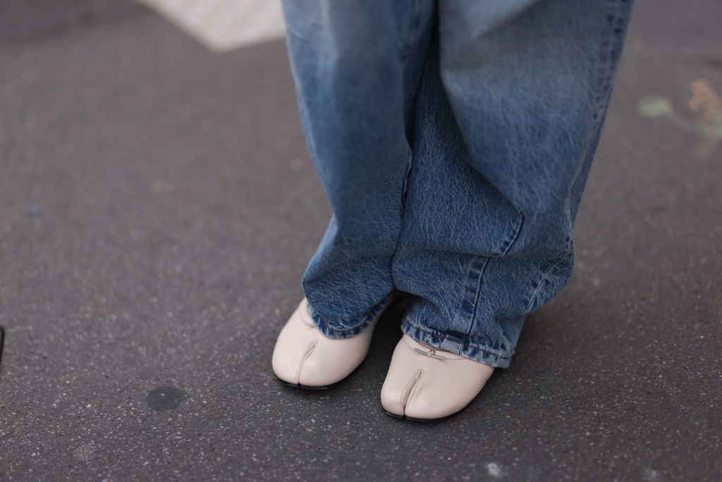 Person wearing loose jeans and white split-toe shoes standing on a pavement