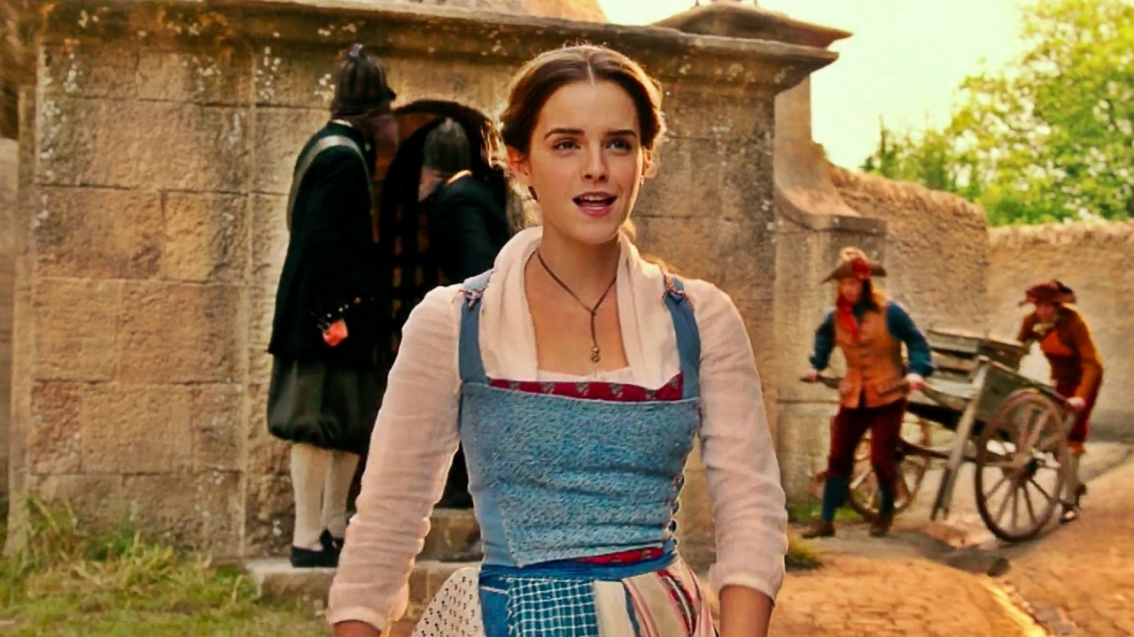Emma Watson as Belle in Beauty and the Beast, wearing a peasant-style dress in front of a village backdrop
