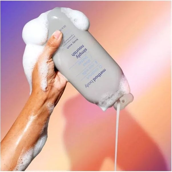 A model's hand holding Method The Body Wash bottle, foaming with soap, highlighting the product in use