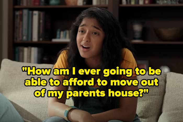 Maitreyi Ramakrishnan sits on a couch, wearing a short-sleeved shirt under green overalls. She appears to be in conversation, leaning slightly forward