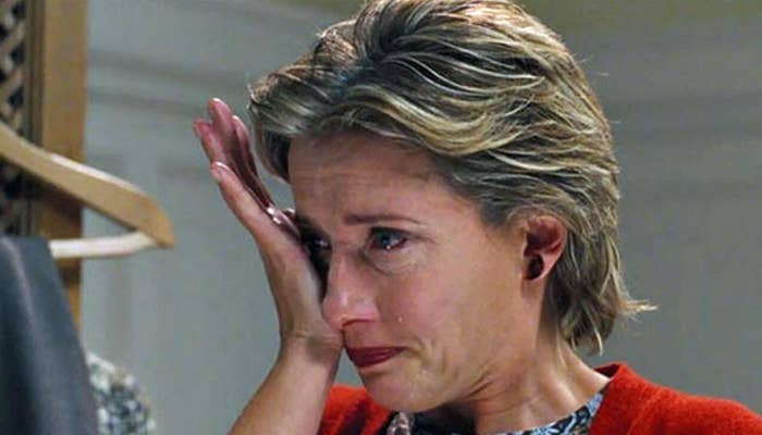 A woman wipes a tear from her eye, appearing emotional while indoors