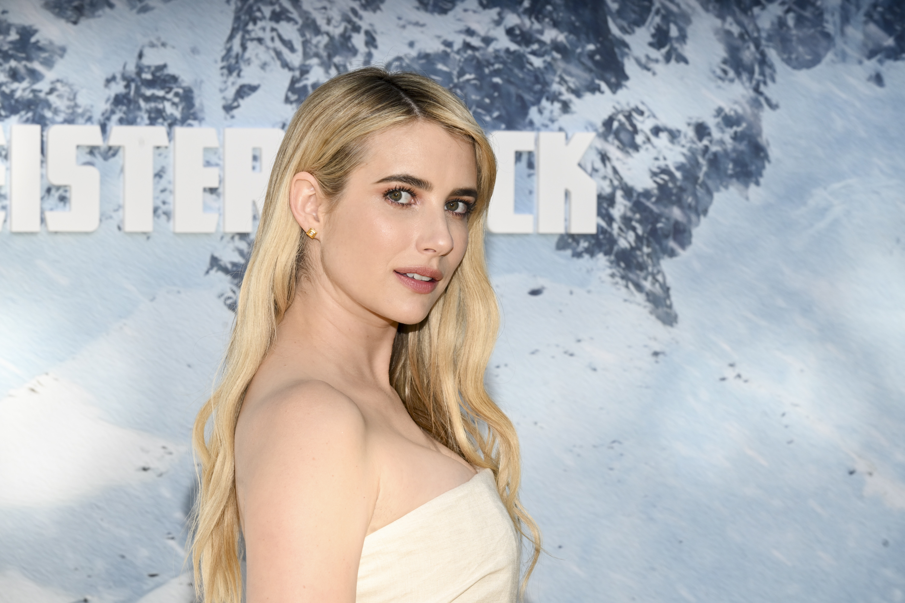 Emma Roberts poses on the red carpet in an elegant, strapless dress, with a snowy mountain backdrop