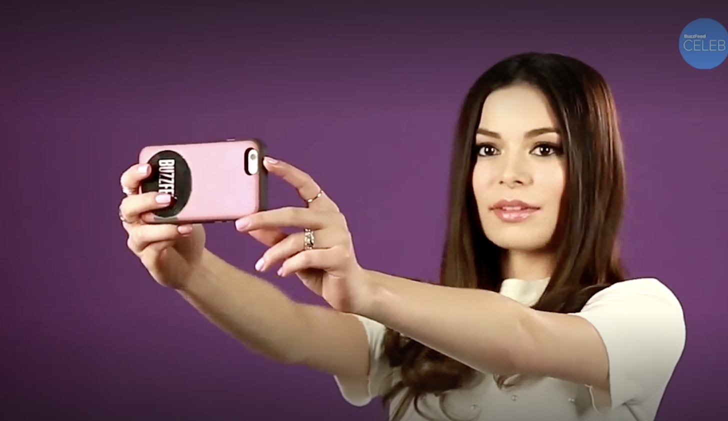 Miranda Cosgrove taking a selfie with her phone against a purple background