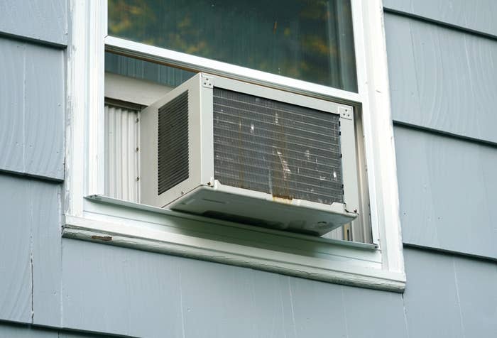 A window air conditioning unit is installed in a partially open window of a house