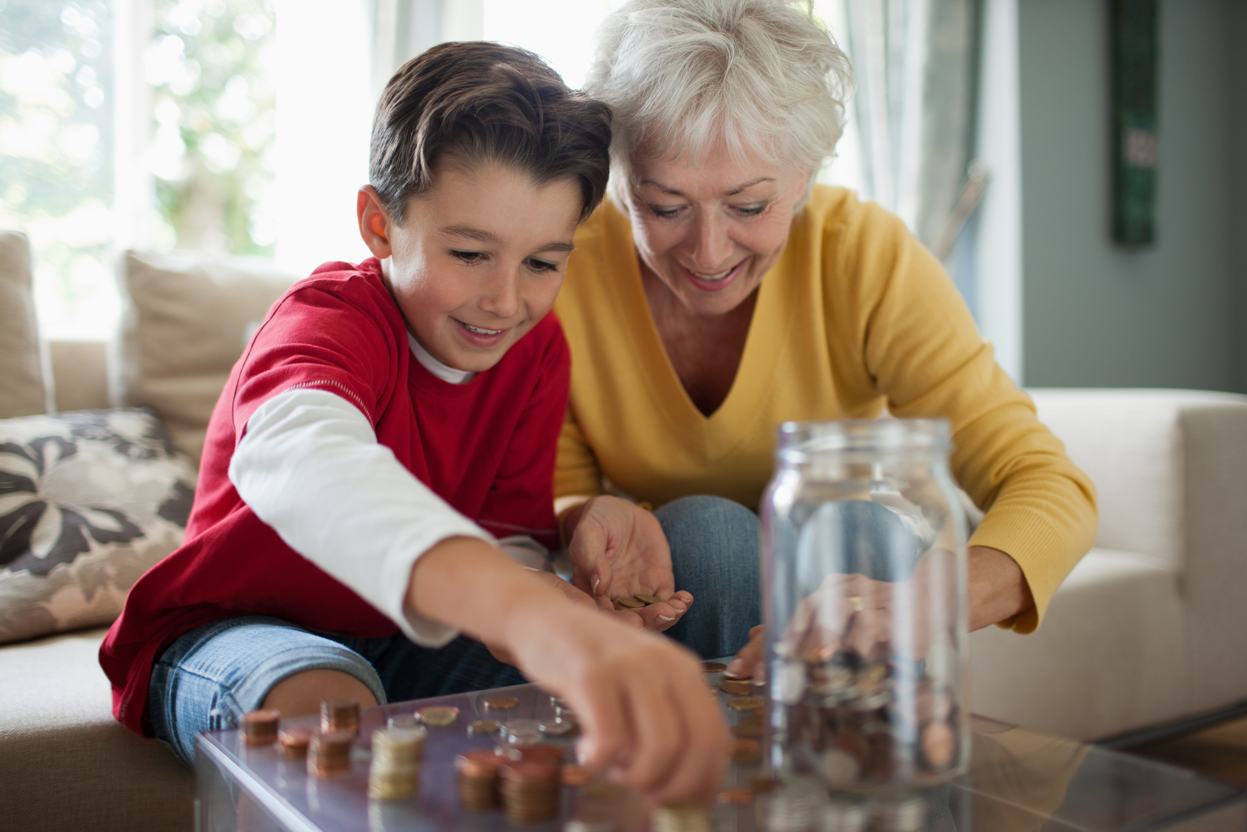 Grandmother and young boy sorting coins on a coffee table, both smiling and engaged in the activity