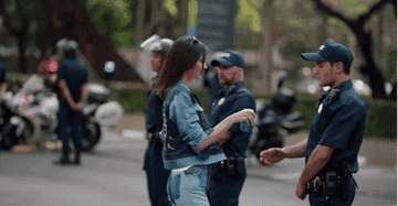 Woman in casual denim outfit getting a wristband from a uniformed police officer at an outdoor event with more officers and motorcycles in the background