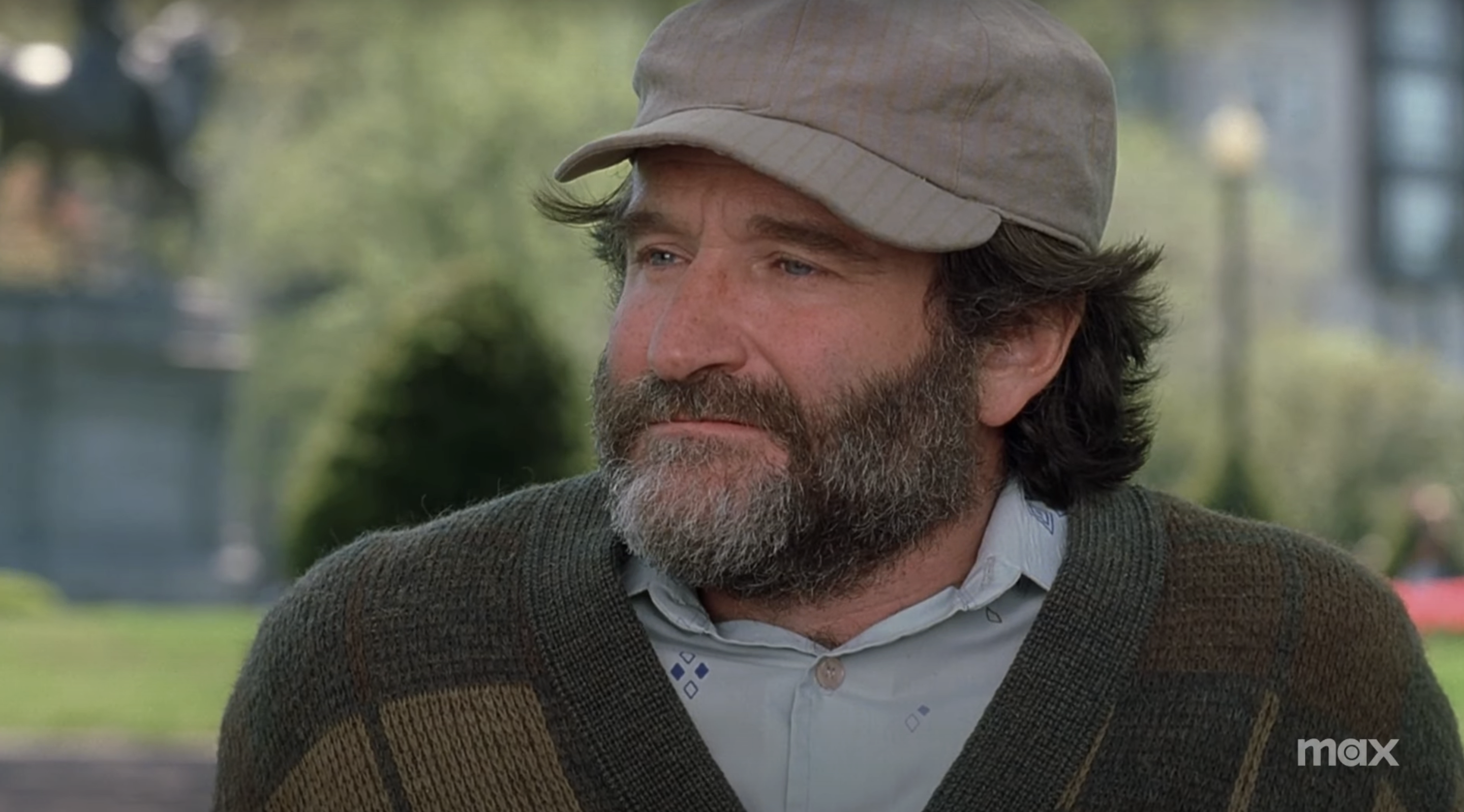 Robin Williams in a scene outdoors, wearing a hat, shirt, and cardigan.