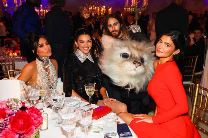 Kim Kardashian, Kendall Jenner, Jared Leto in a cat costume, and Kylie Jenner at a formal event, seated at a table with elegant dinner settings