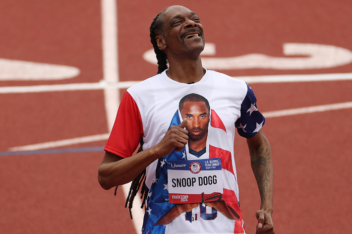 Snoop Dogg celebrates on a track, wearing a shirt featuring Kobe Bryant’s image draped in an American flag