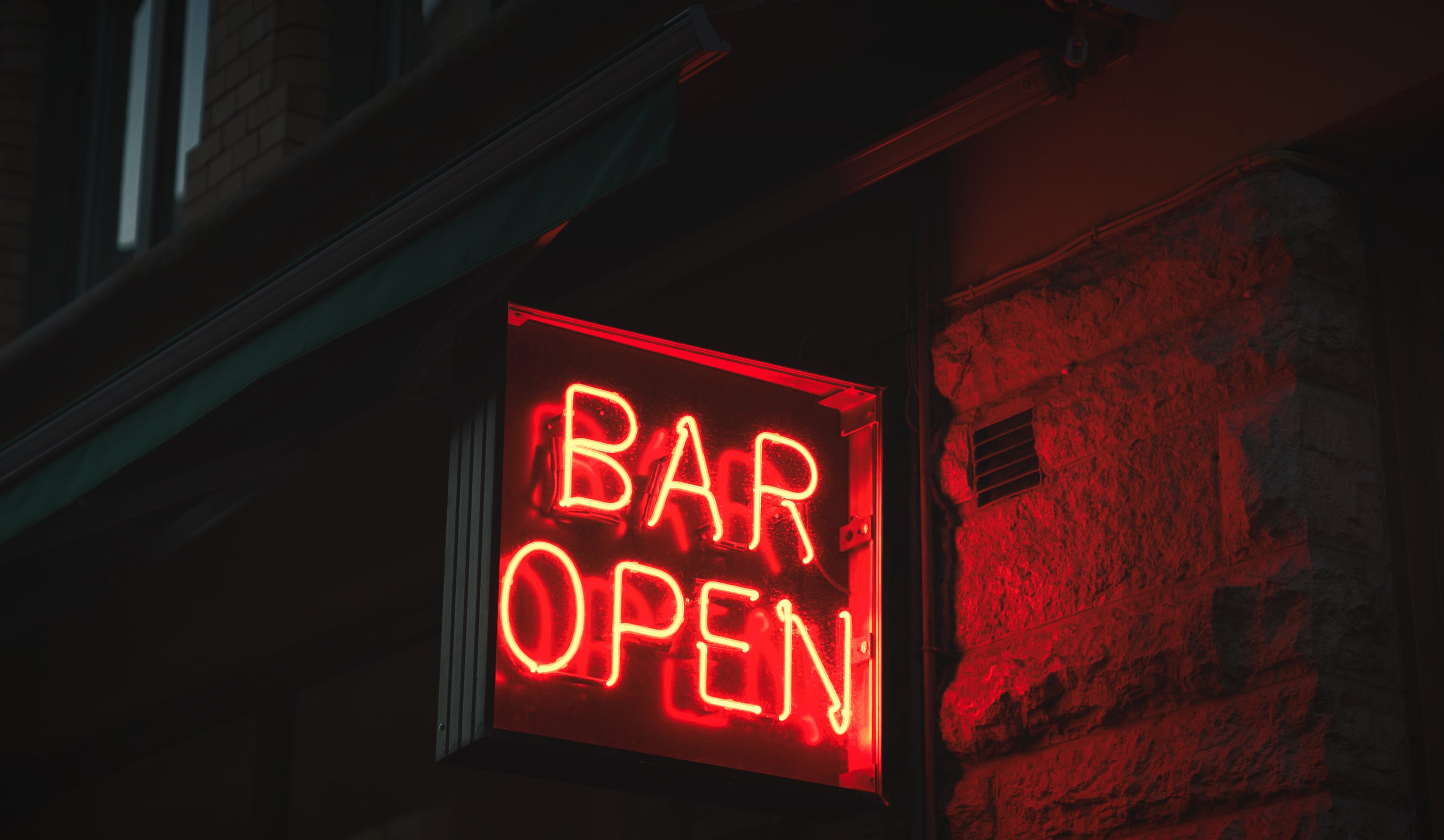 Neon sign reads "BAR OPEN" outside a brick building at night