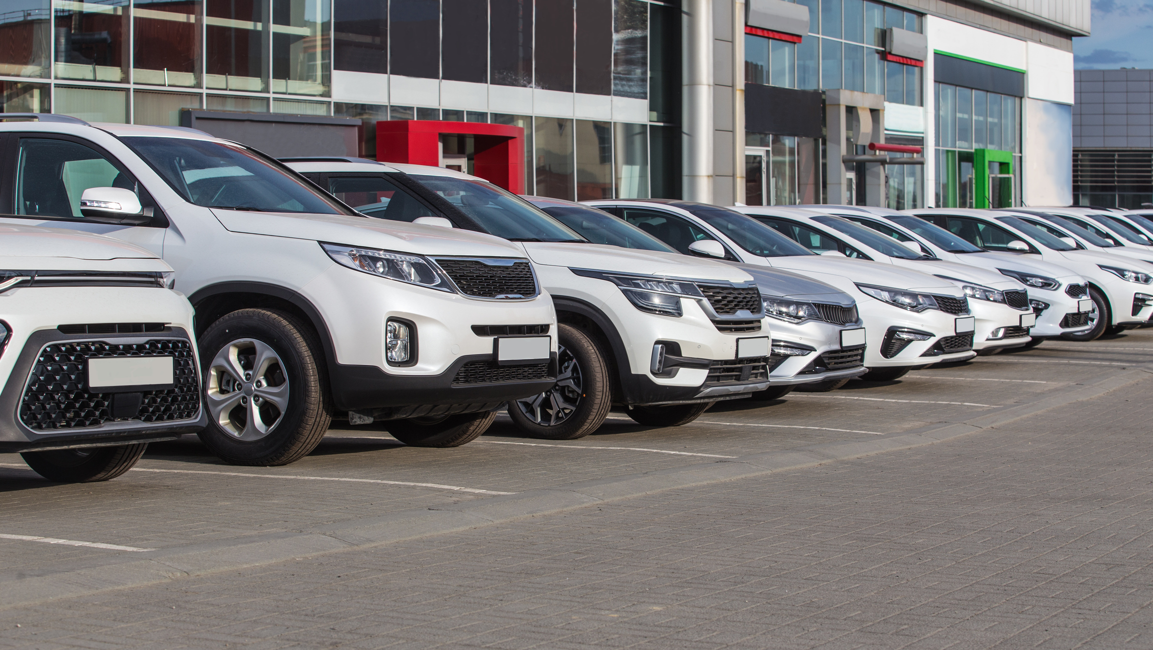 A line of white SUVs and cars parked in a lot in front of a modern commercial building