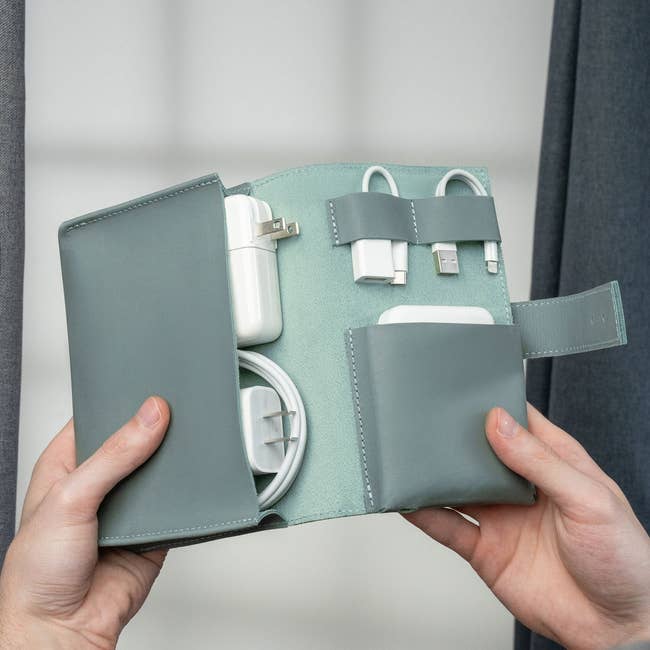 Hands holding a compact travel case containing various electronic chargers and cables, organized neatly in dedicated compartments