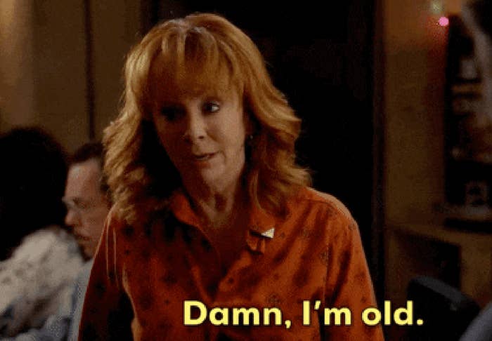 Woman with red hair in patterned shirt exclaiming, "Damn, I'm old." Background includes another person and some furnishings