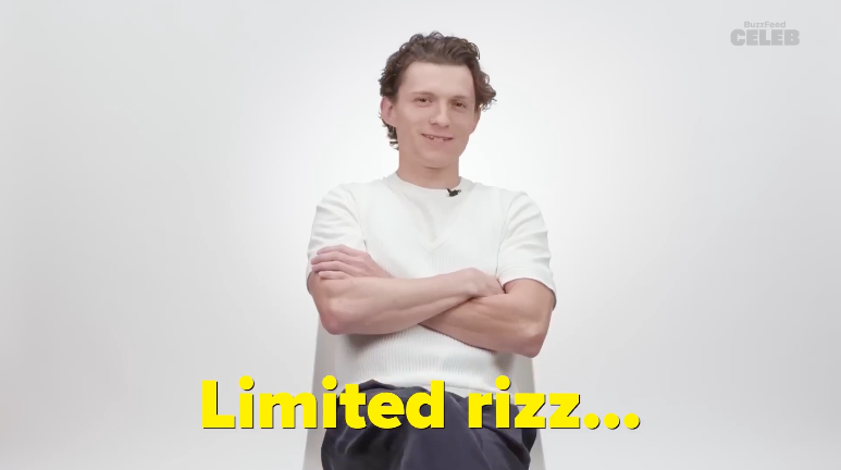 Tom Holland sits in a chair with arms folded, wearing a casual light shirt and dark pants. The text at the bottom reads, "Limited rizz…"
