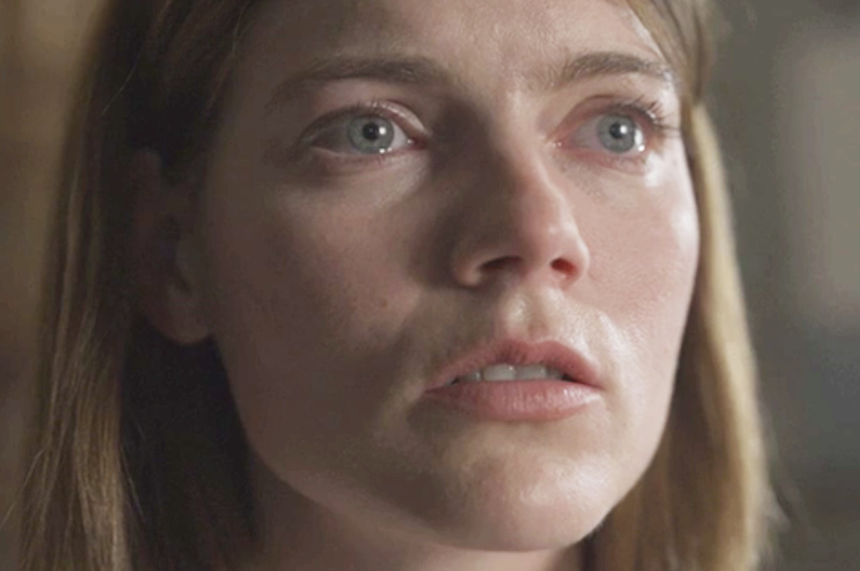 Close-up of a woman with light brown hair and teary blue eyes, looking slightly upwards with a somber expression