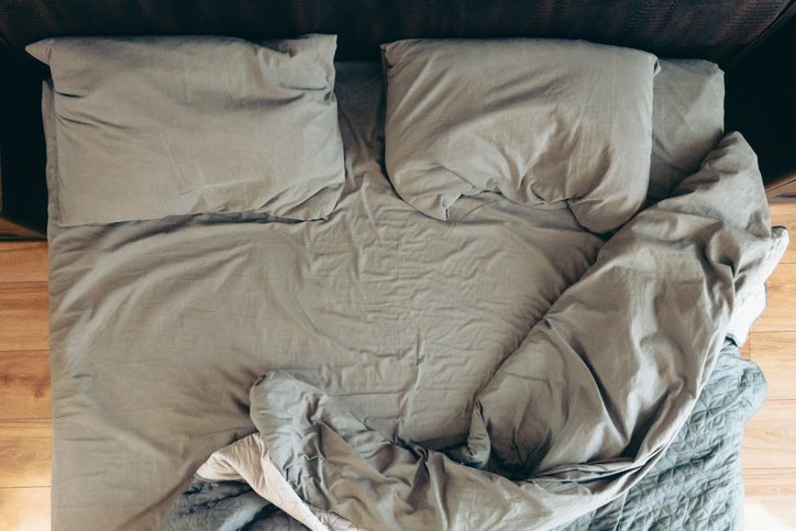 Top-down view of a rumpled bed with two pillows and a blanket