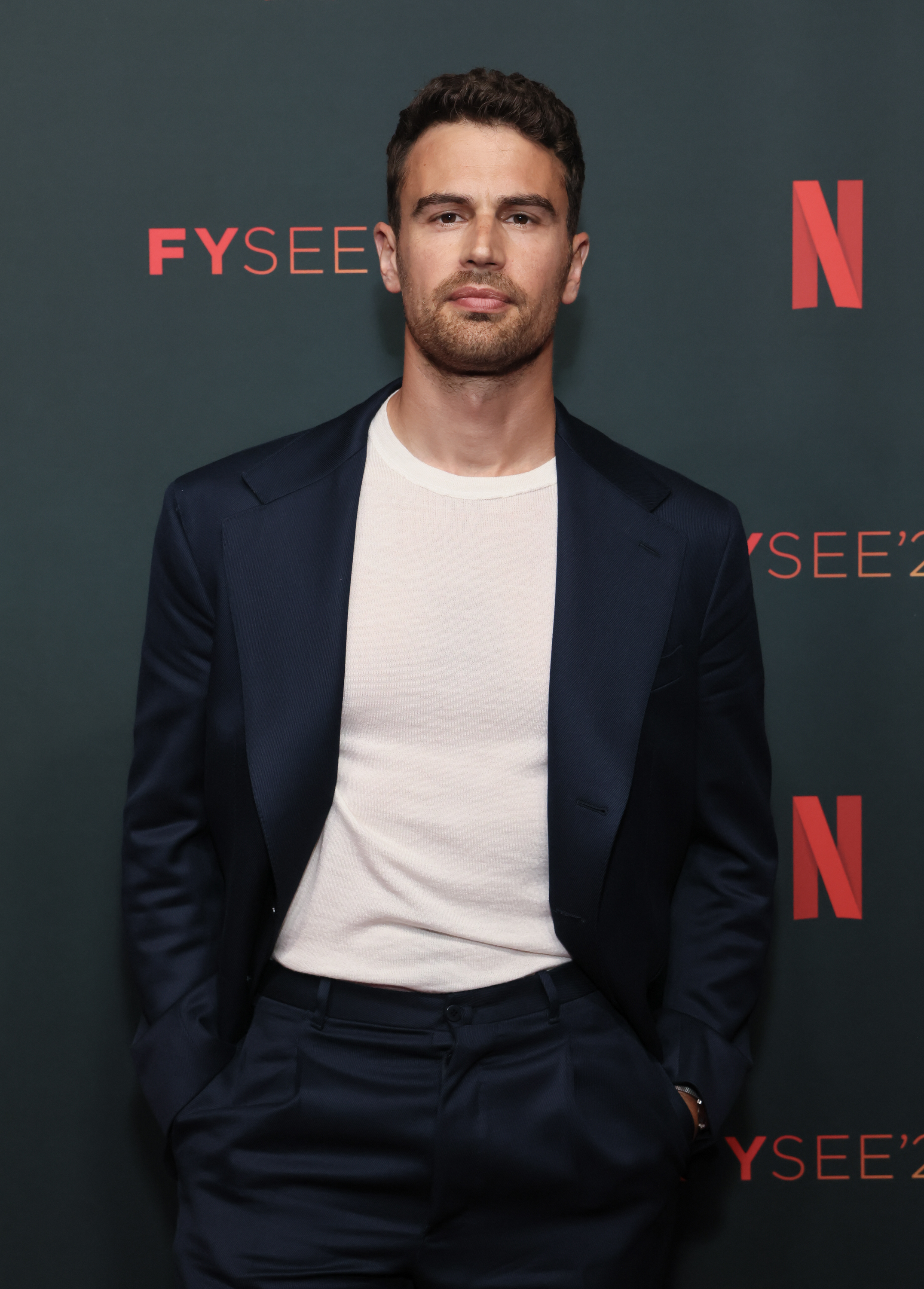 Theo James poses in a navy blazer and white shirt at Netflix's FYSEE event