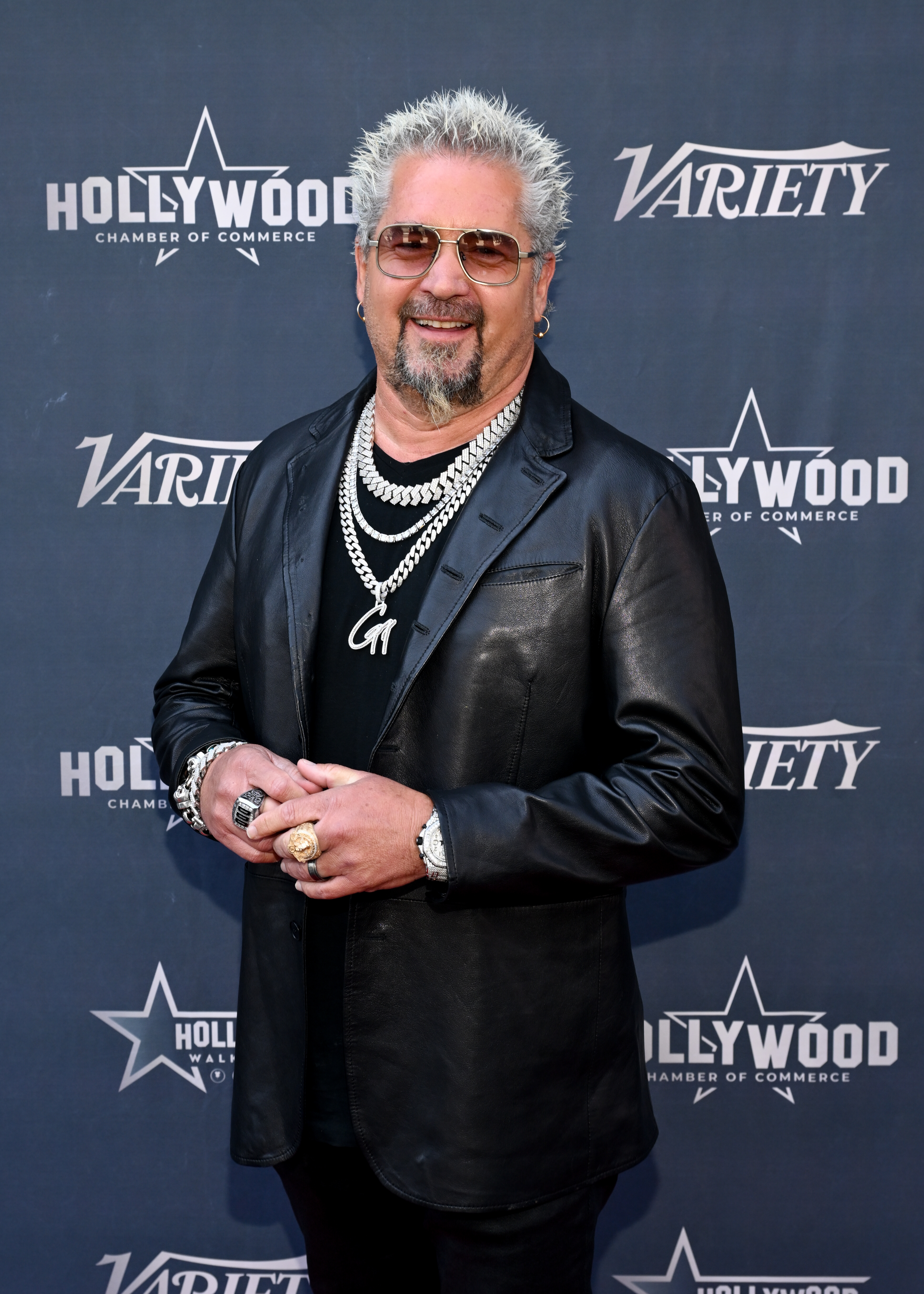 Guy Fieri at a Hollywood Chamber of Commerce Variety event wearing a black leather jacket, black shirt, dark sunglasses, and silver chain necklaces