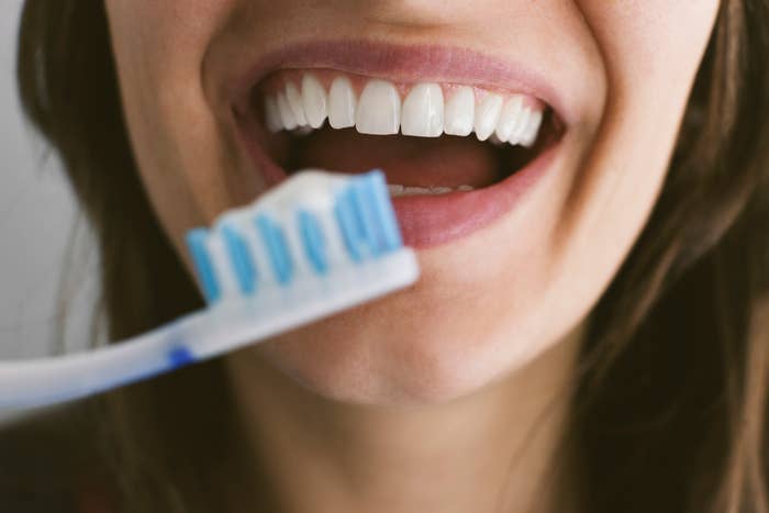 Close-up of a smiling person brushing their teeth. The focus is on the toothbrush and their teeth