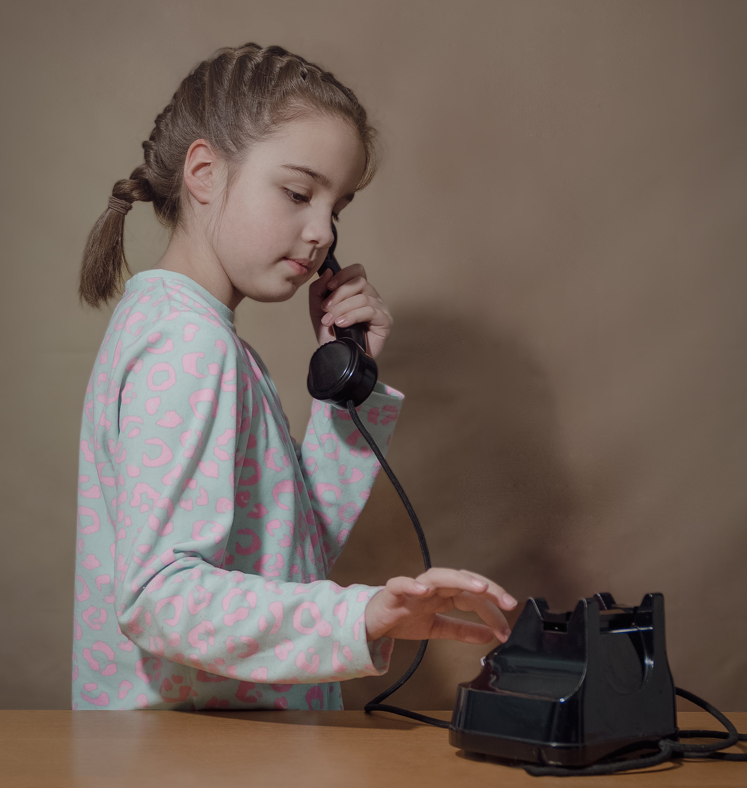 Girl with braided hair in pajamas holding a vintage phone handset and dialing a number on the rotary dial