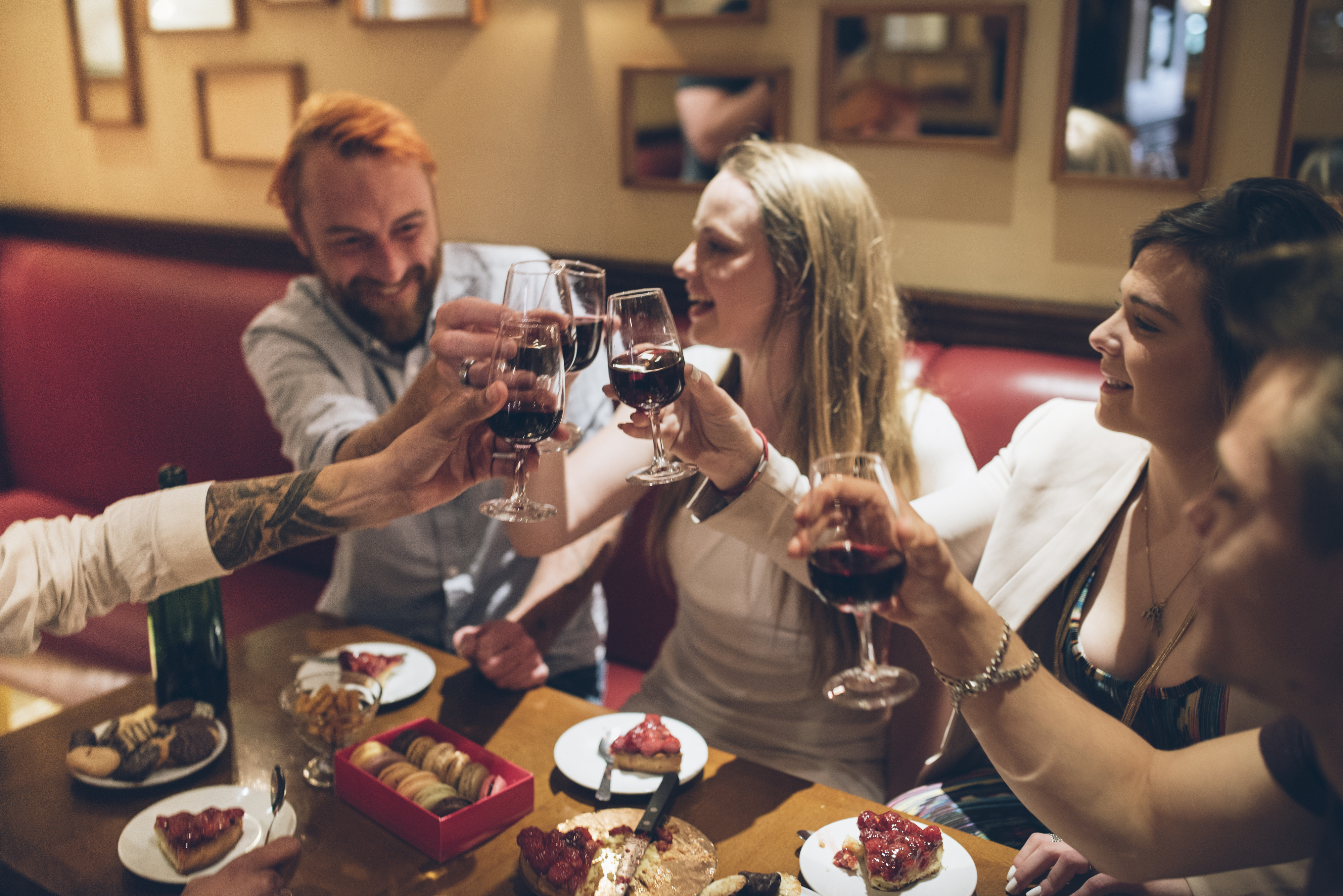 A group of five people toasting with wine glasses at a dining table, enjoying desserts and snacks in a cozy setting.
