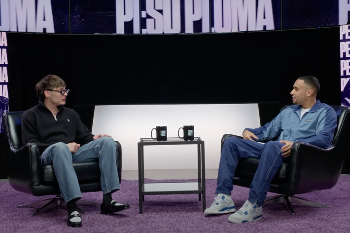 Roddy Ricch in a blue tracksuit and black sneakers appears in an interview with MrBeast, who is wearing a black sweater and jeans, seated on a stage with P:SOPUMA branding