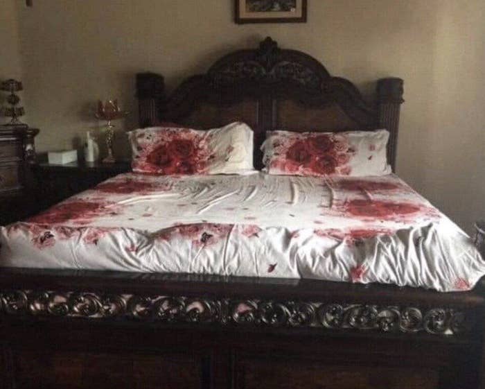 A bed with a carved wooden headboard, floral-patterned bedding, and matching pillows is neatly made in a traditional-style bedroom