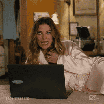 Annie Murphy, wearing a robe, is lying on a bed with a shocked expression while looking at a laptop screen in a scene from &quot;Schitt's Creek&quot; and says, &quot;Yum!&quot;