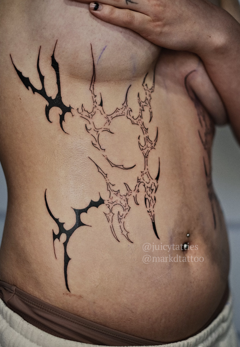 A detailed geometric tattoo design on a person's ribcage with the Instagram handles @juicytatties and @markdtattoo visible near the tattoo