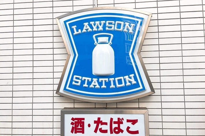 青い看板に白い牛乳瓶のロゴが描かれたLAWSON STATIONの看板と、その下に「酒・たばこ」と書かれた赤い文字の看板。