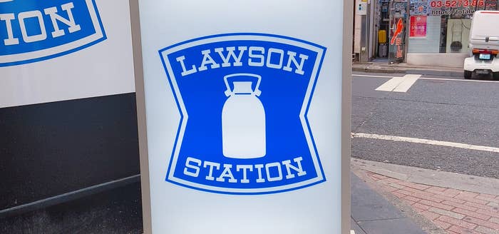 ローソンステーションの青いロゴが描かれた看板。背景には街中の風景が見える。