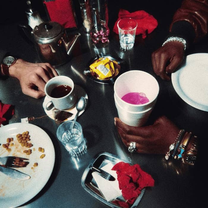 A table with an assortment of items including drinks, a plate with food remnants, utensils, jewelry on hands, and various other items, no person fully visible