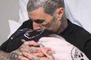 Travis Barker embraces and kisses baby Rocky wrapped in a blanket.
