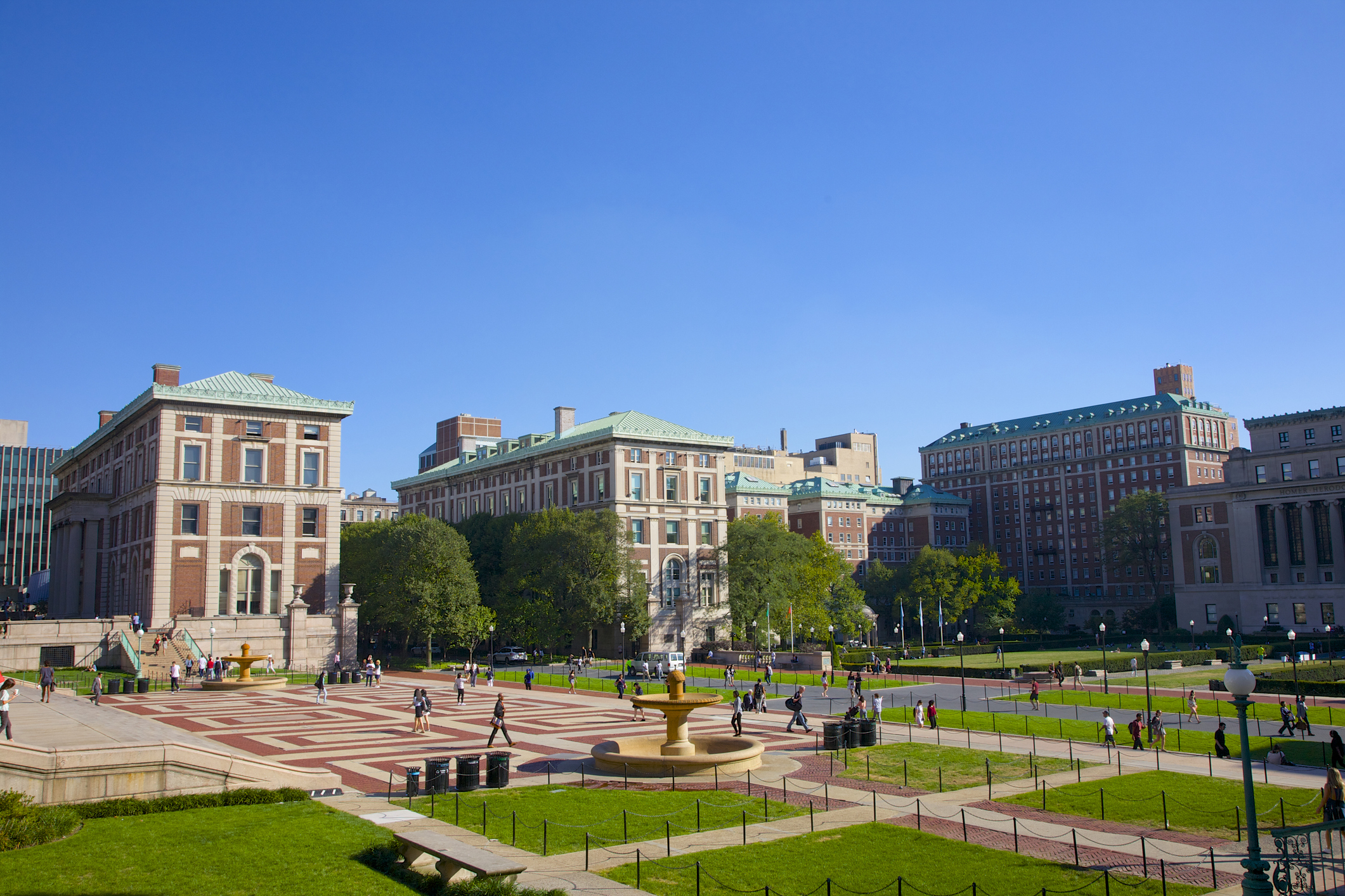 View of a university campus courtyard with people walking and socializing, surrounded by large academic buildings