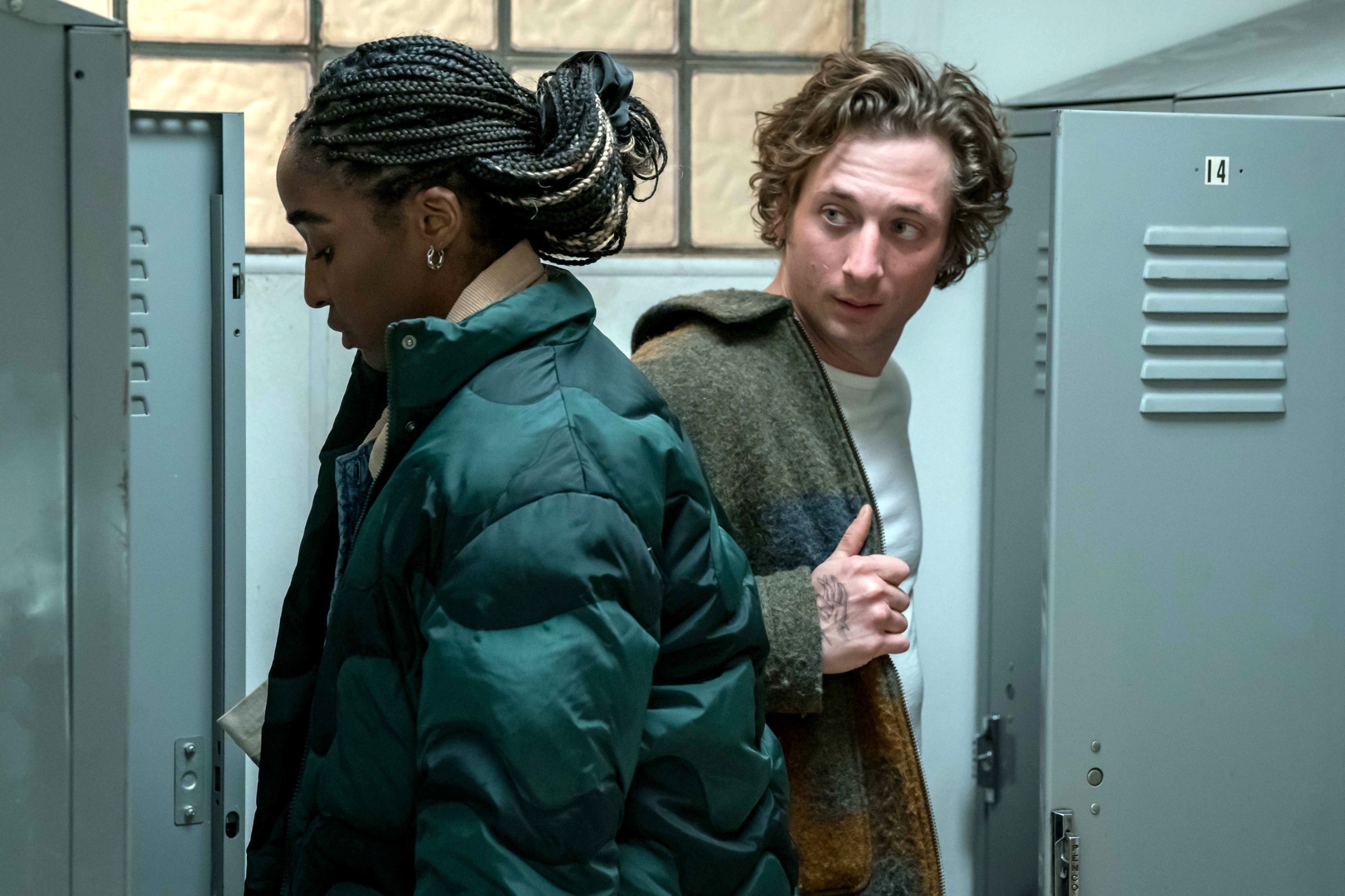 Ayo Edebiri and Jeremy Allen White in a still from a scene, with Edebiri opening a locker and White looking at her dressed in casual winter clothing