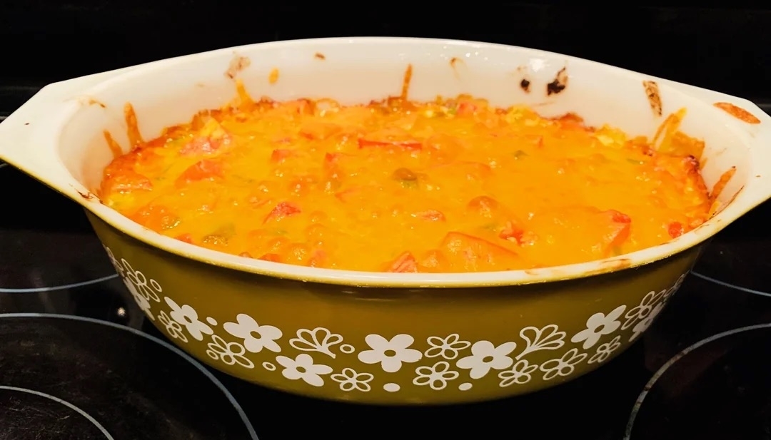 A casserole dish filled with a cheesy, baked dish, likely containing vegetables, sits on a stove