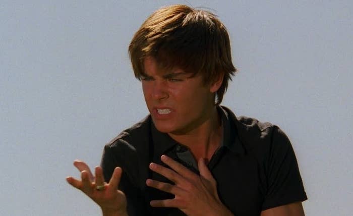 Zac Efron in a tense scene from a movie. He is holding one hand out while the other hand rests on his chest. His expression appears intense and determined