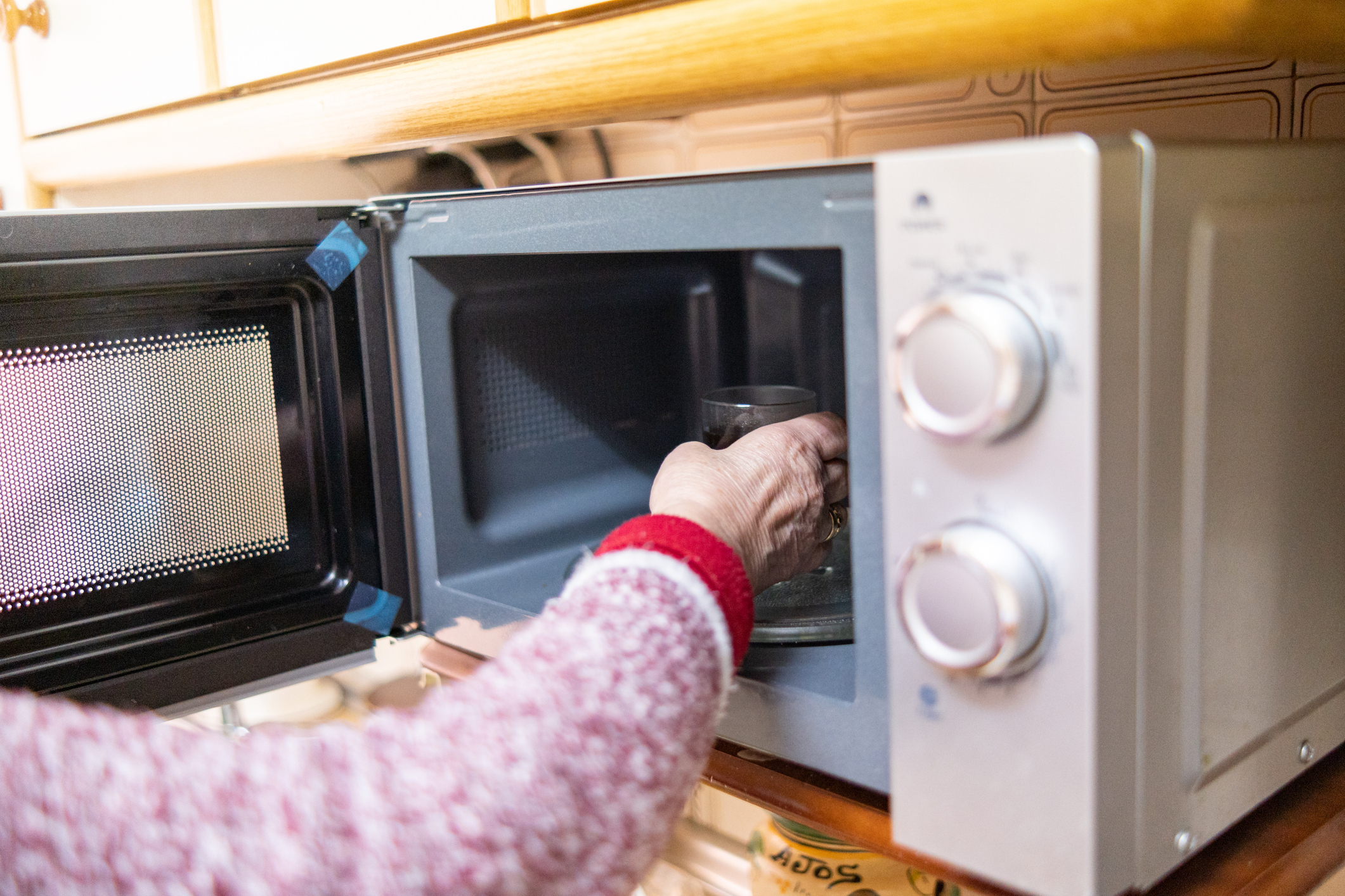 A person with a red and white sweater places a glass container into a microwave in a kitchen setting
