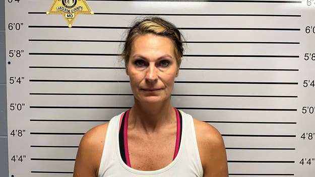 A woman wearing a sleeveless top stands in front of a height chart for a mugshot. The Laclede County, MO sheriff's badge is on the upper left
