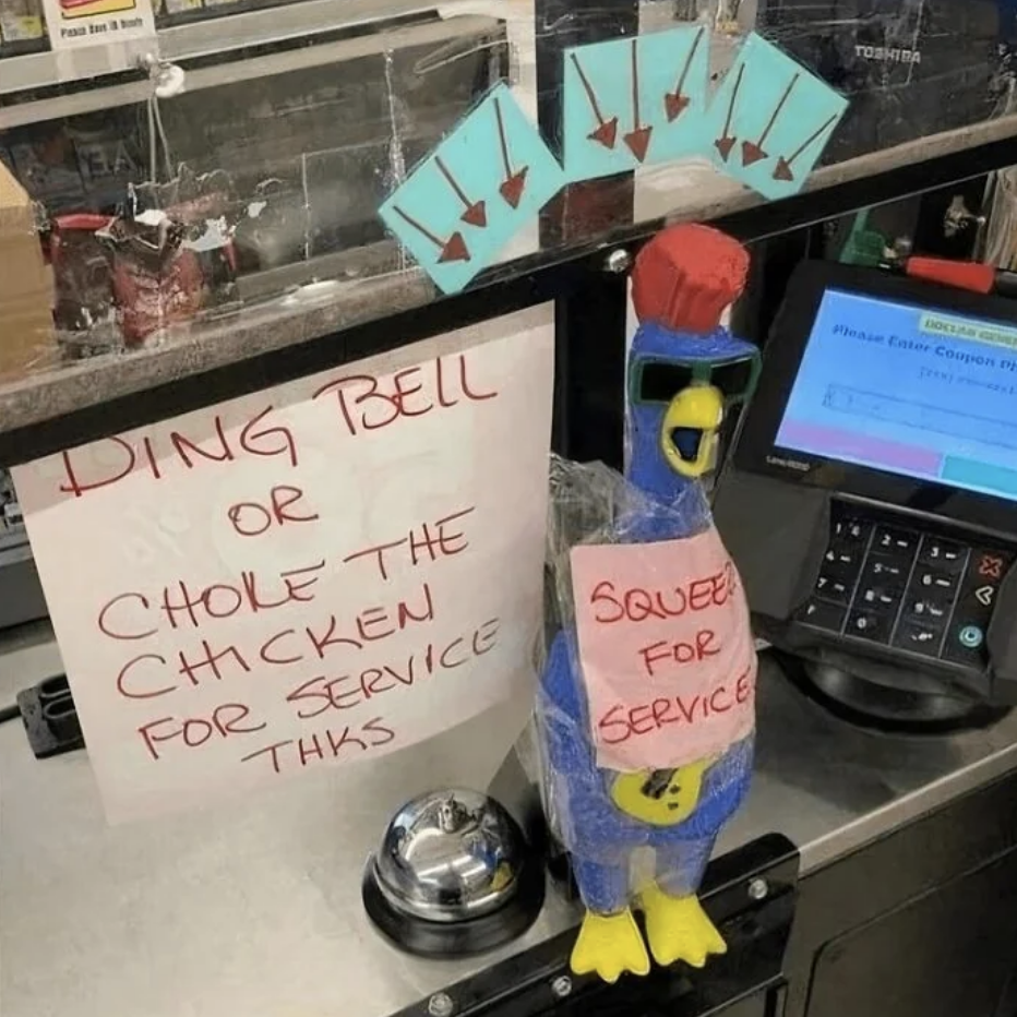 Counter with note reading &quot;Ding bell or choke the chicken for service thks,&quot; rubber chicken wearing a red cap with a &quot;Squeeze for service&quot; sign, bell and register