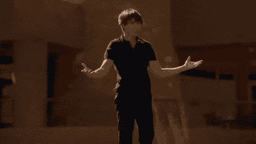 Zac Efron, in casual attire, performs an expressive dance move outdoors with arms spread