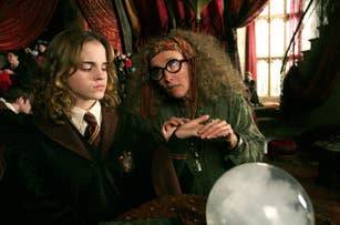 Emma Watson, dressed in a Hogwarts uniform, sits while Emma Thompson, in eccentric attire with a headscarf, examines her palm in a scene from the Harry Potter series