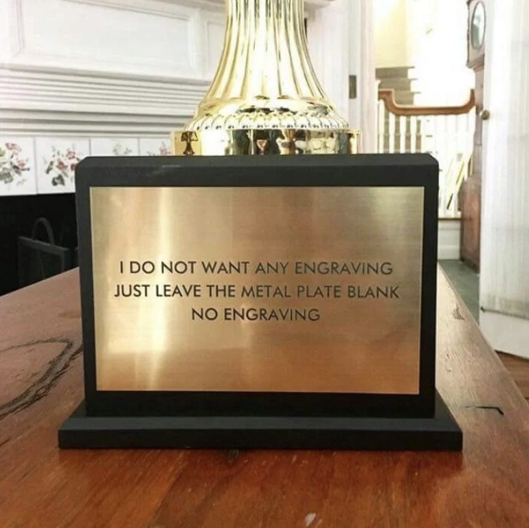 A gold trophy with a metal plate that reads: "I DO NOT WANT ANY ENGRAVING JUST LEAVE THE METAL PLATE BLANK NO ENGRAVING."
