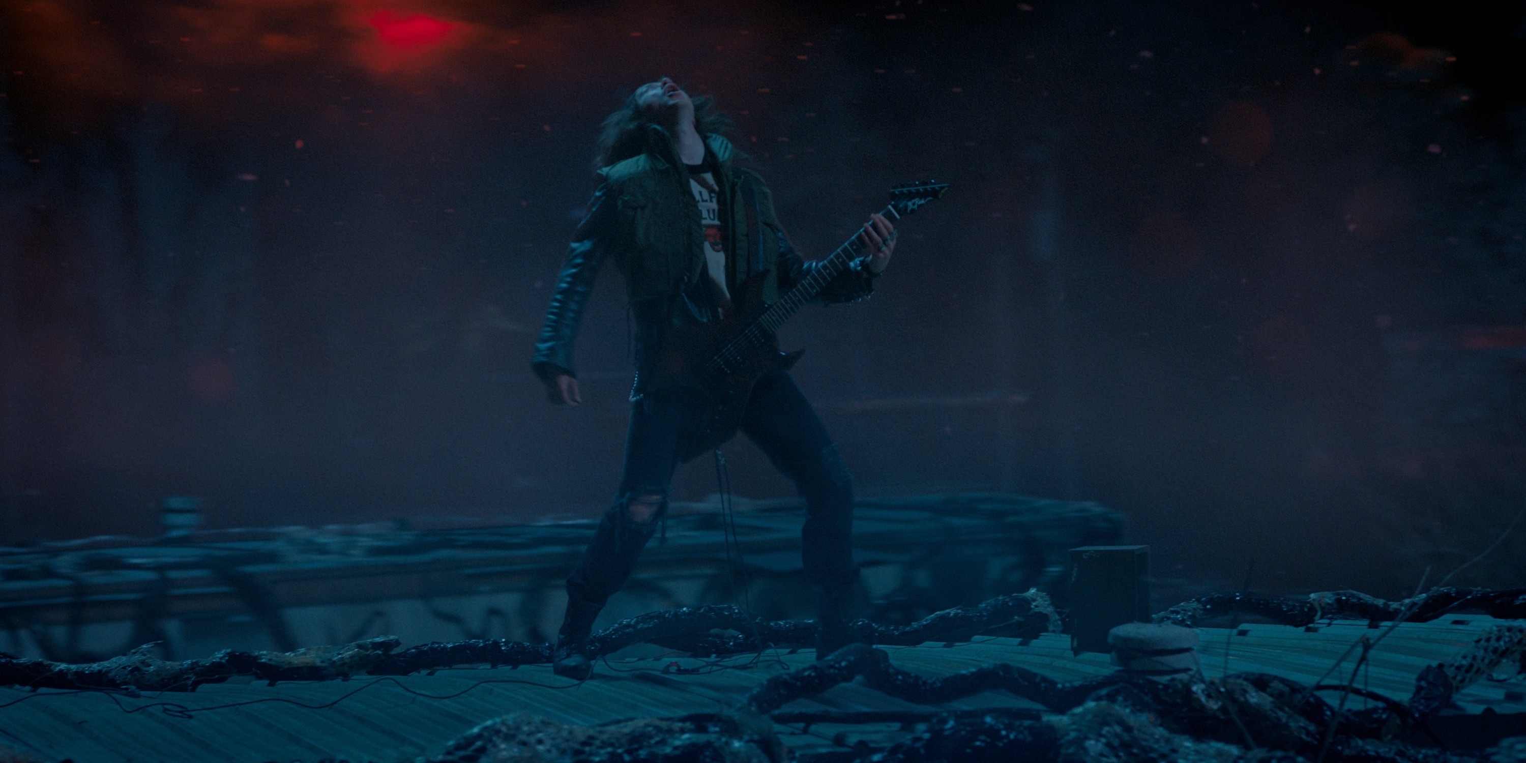 Eddie Munson from Stranger Things, wearing a leather jacket and playing a guitar on a dark, eerie stage with red lighting