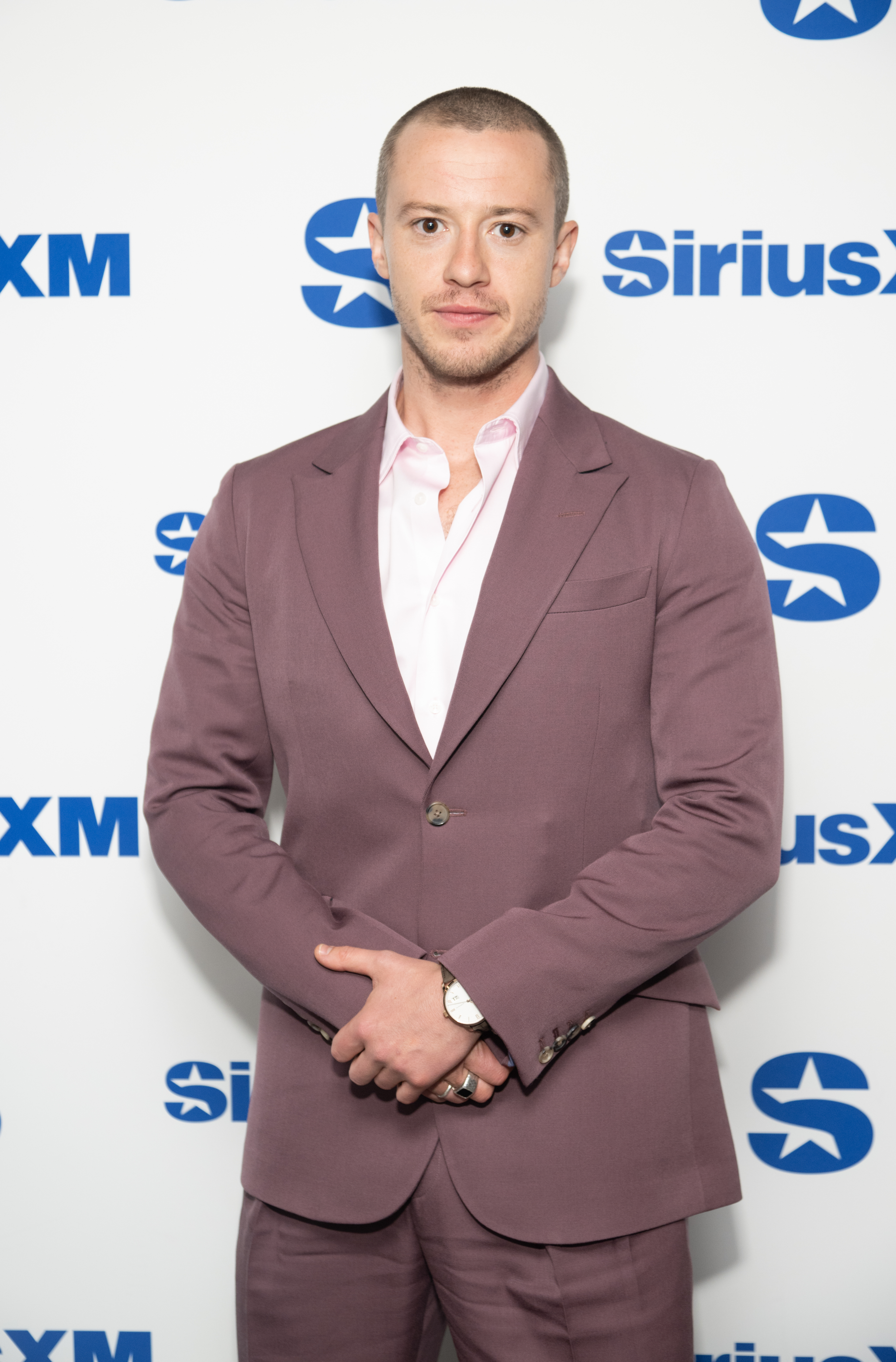 Joseph Quinn in a mauve suit poses at a SiriusXM event