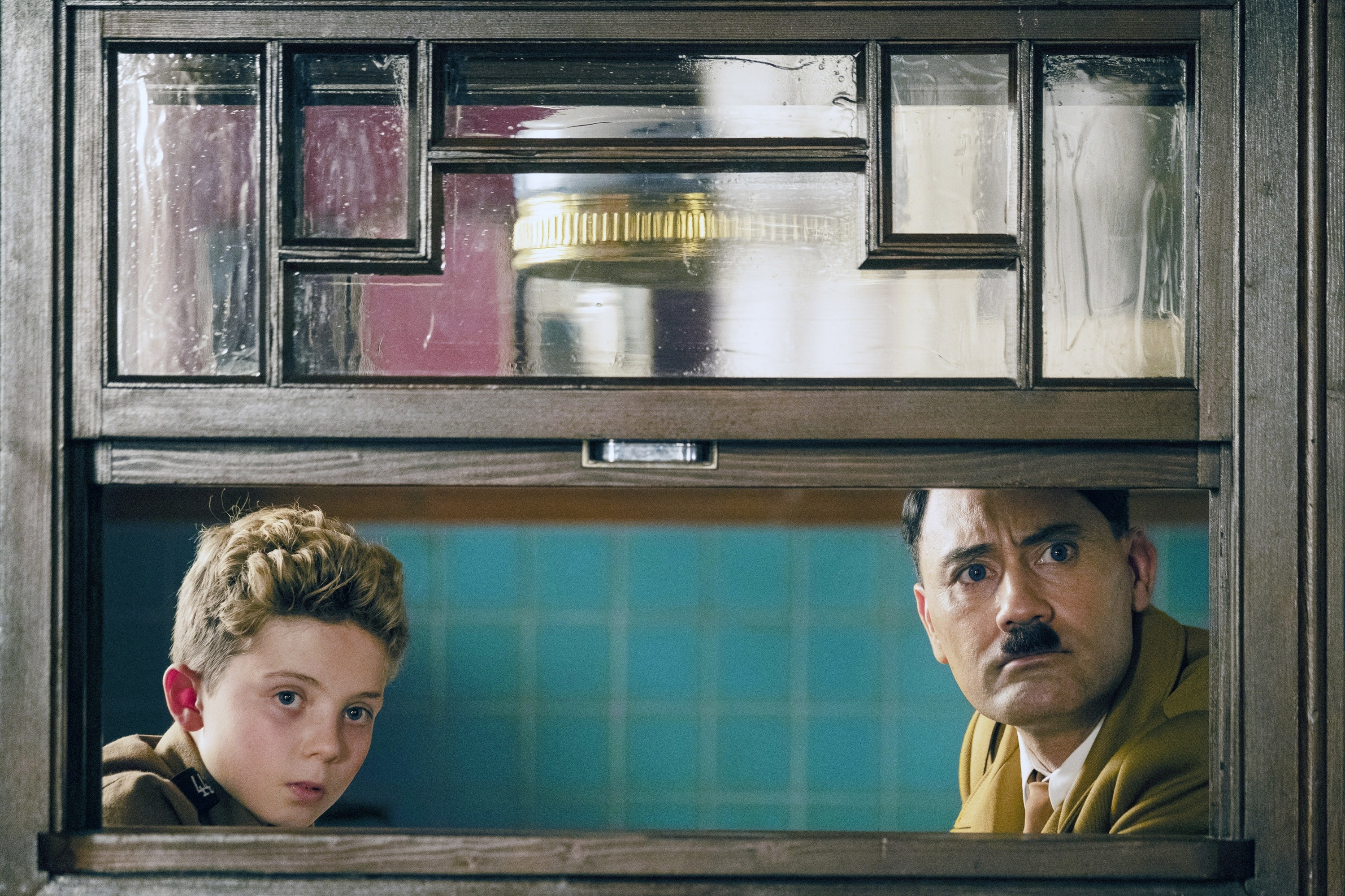 Roman Griffin Davis and Taika Waititi are peering through a window in a scene from the movie "Jojo Rabbit."