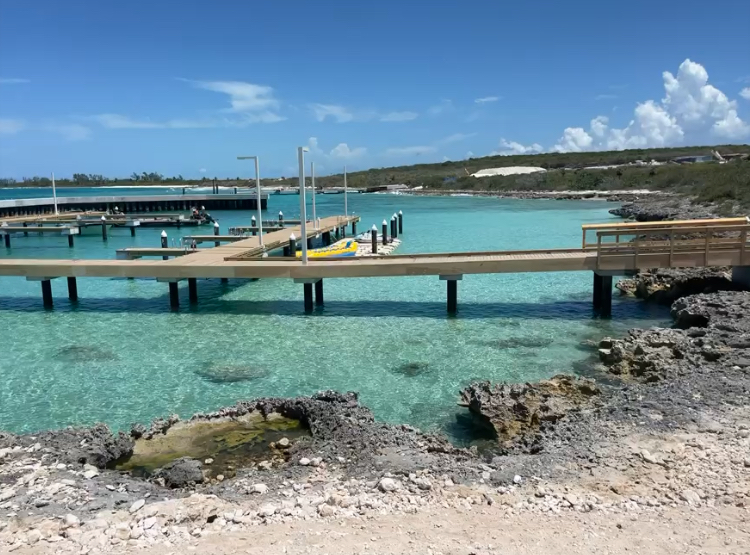 A calm, clear turquoise ocean with several wooden docks extending into the water, set against a backdrop of rocky shore and blue sky