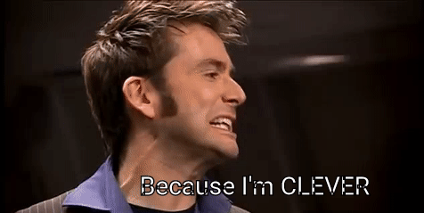 David Tennant in character, wearing a pinstripe suit with a blue shirt, passionately saying, "Because I'm CLEVER."